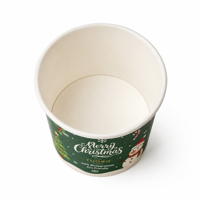 Top view product photo of empty TUOBO green Christmas biodegradable paper ice cream cup with natural white inner liner, full custom Merry Christmas snowman tree print, compostable disposable dessert tub for cafe holiday bulk supply