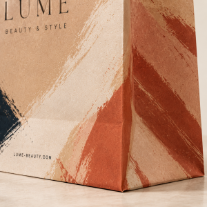 Close-up detail of a luxury abstract brushstroke kraft paper bag corner with textured printing, sharp fold lines, and premium matte finish in warm neutral tones.