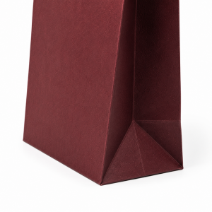 Side view focused on folded triangle bottom side gusset construction of burgundy textured single wine bottle paper gift bag, solid white isolated background, premium grain paper texture display