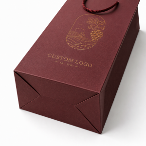 Top-down product detail of folded bottom gusset structure for single wine bottle burgundy textured paper tote bag, golden grape vine embossed foil print on front panel, plain white background