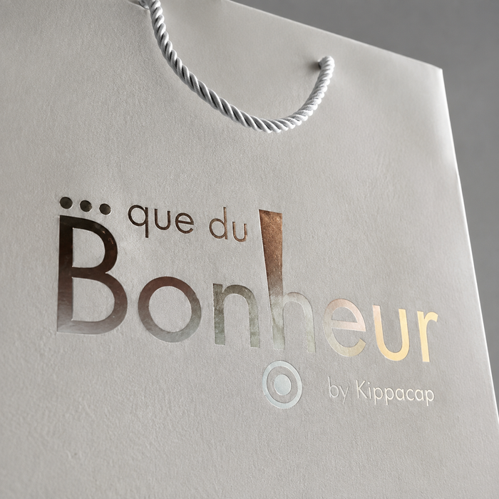 Close-up of elegant metallic foil printed logo on textured paper gift bag with twisted rope handle.