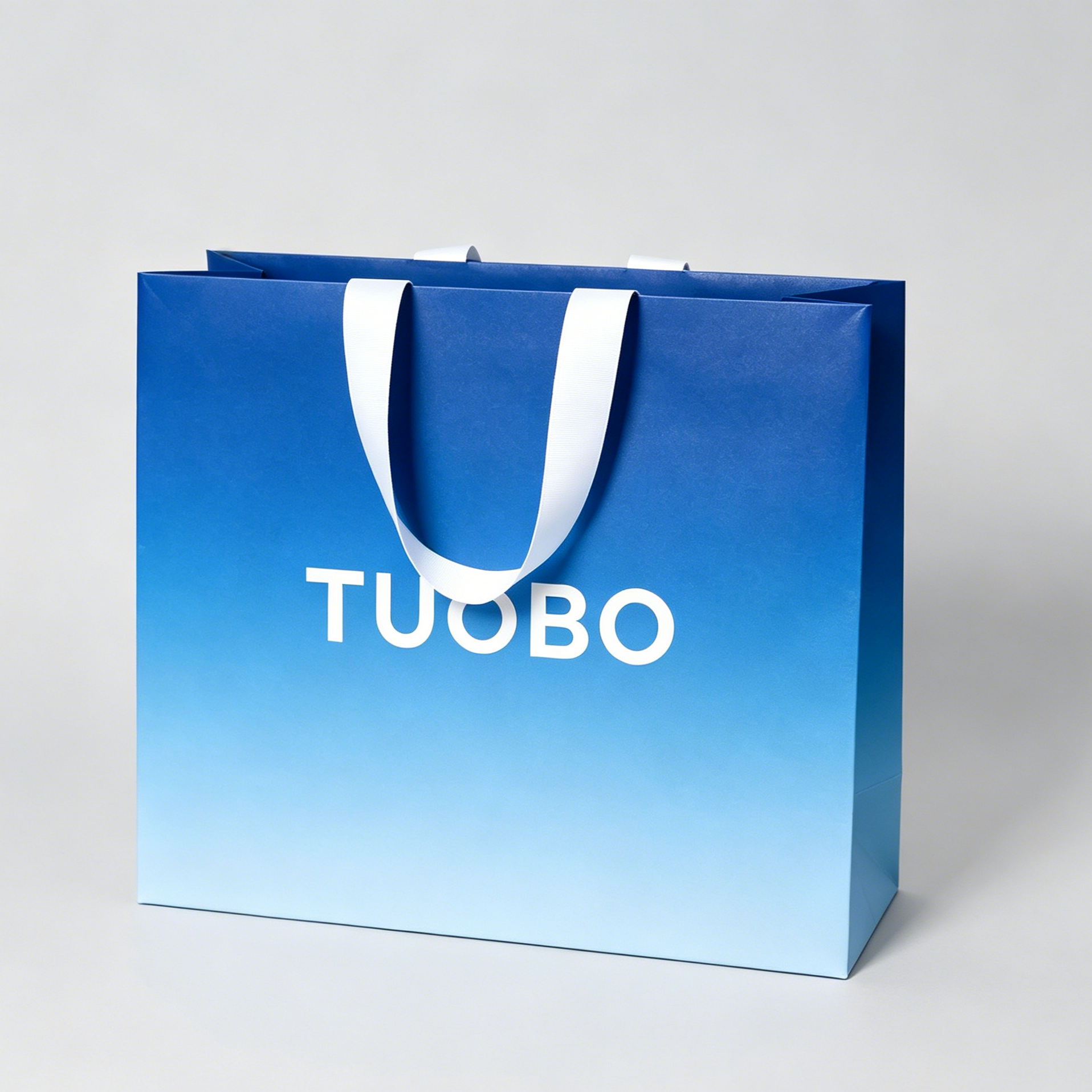 Single matte blue gradient TUOBO branded paper retail bag with internal white ribbon handles, neutral studio background premium fashion packaging render