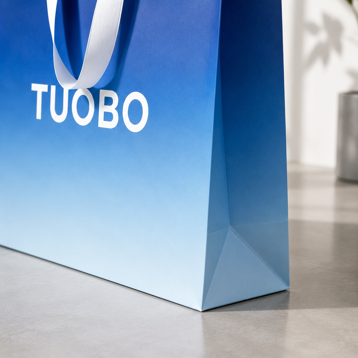 Detail view of sturdy side fold base construction on matte blue TUOBO branded luxury paper tote bag