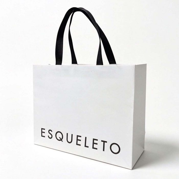 Side view of a white bag with handles and black branded text on a clean white backdrop.