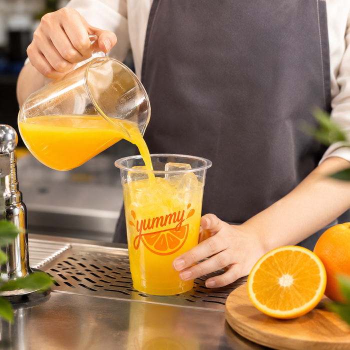 Barista pouring fresh orange juice into custom printed rPET clear plastic juice cup, recycled PET recyclable cold drink takeaway cups, sustainable cafe juice bar packaging