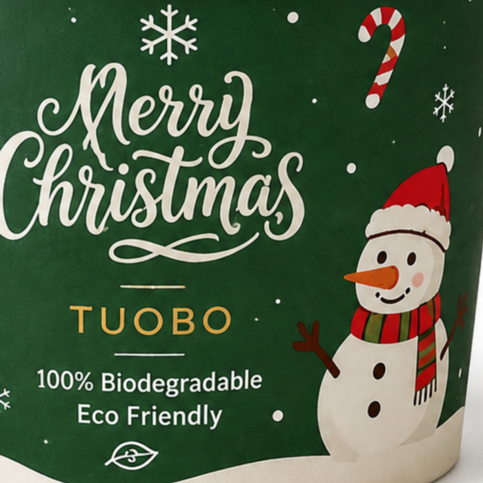 Macro close-up shot of TUOBO green Christmas biodegradable paper ice cream cup printed surface, featuring Merry Christmas lettering, snowman, candy cane and snowflake pattern, 100% biodegradable eco friendly disposable frozen yogurt cup for wholesale holiday dessert packaging