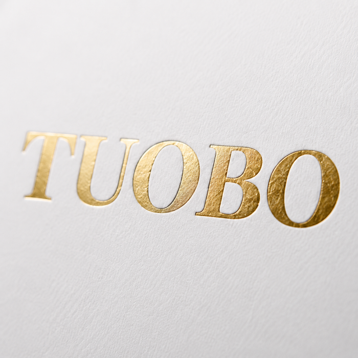 Macro close-up shot of a metallic gold foil printed logo on high-texture white matte paper packaging.