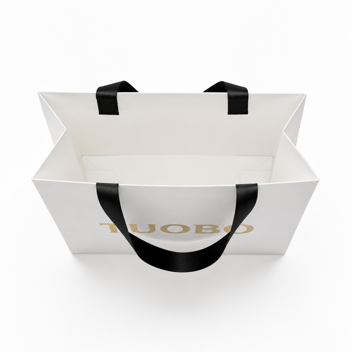 Overhead top view showing the spacious interior and black ribbon handles of an open white paper gift bag.
