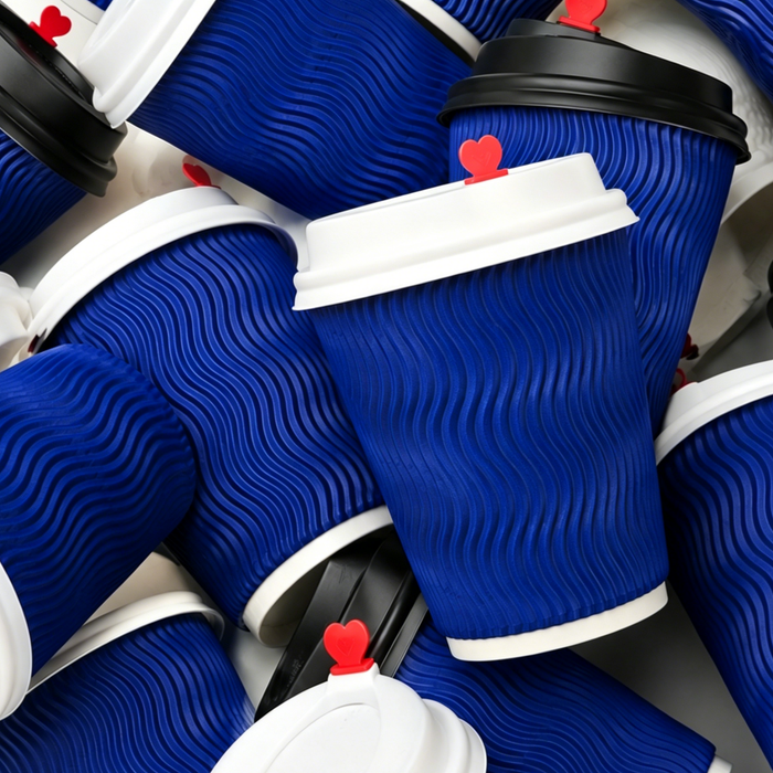 Flat lay stacked shot of multiple blue ripple wall paper cups with white and black lids with red heart stoppers, biodegradable PLA lined insulated disposable coffee cups, stackable eco friendly takeaway ripple wall cups for foodservice wholesale supplier