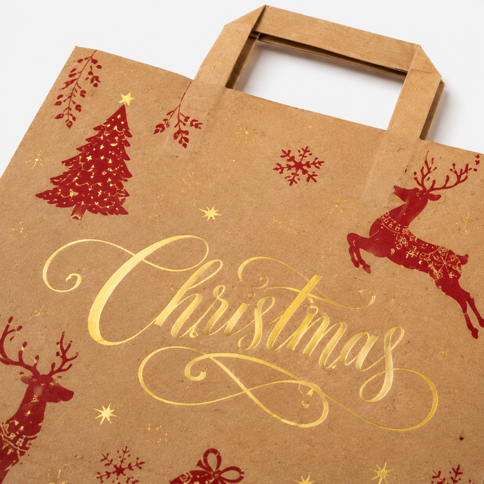 Detailed view of brown kraft paper Christmas gift bag showing gold foil 'Christmas' script, red reindeer and tree motifs, highlighting metallic finish on white background.
