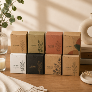 Collection of custom printed kraft paper tuck top tab lock boxes in various earthy tones with botanical line art designs for scented candle packaging, neatly arranged on a wooden table.